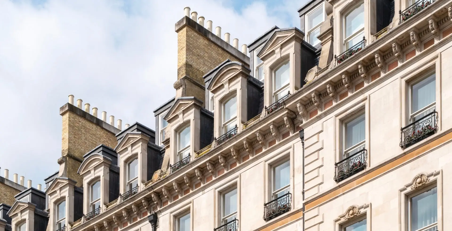 Belgravia houses with white rooftops and many windows on a sunny and cloudy day.